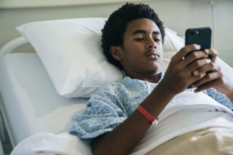 Black boy laying in hospital bed texting on cell phone