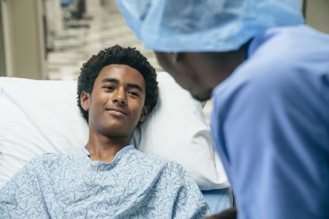 Black doctor talking to boy in hospital bed