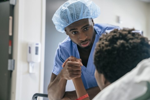 Black doctor holding hand of boy in hospital bed