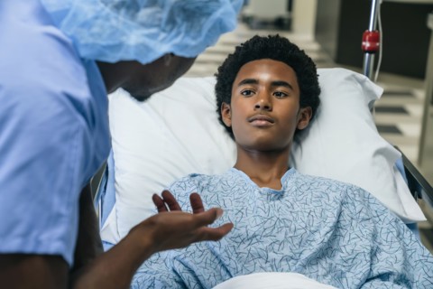 Black doctor talking to boy in hospital bed