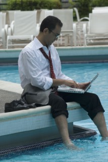 Hispanic businessman using laptop next to swimming pool
