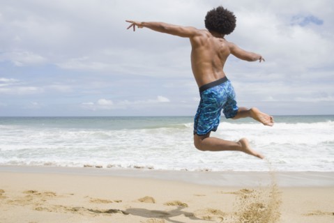 African man at beach jumping in mid-air
