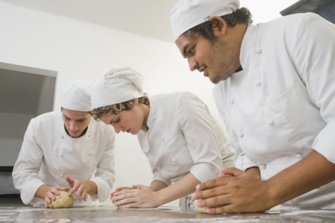 Bakers working with dough in bakery kitchen