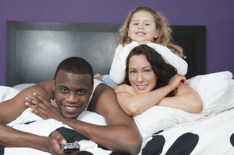 Family laying in bed together watching television