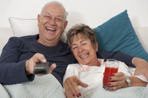 Senior Hispanic couple laying in bed watching television