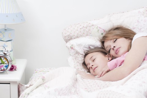 Hispanic mother and daughter sleeping together in bed