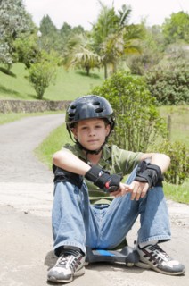 Hispanic boy in pads and helmet sitting on skateboard