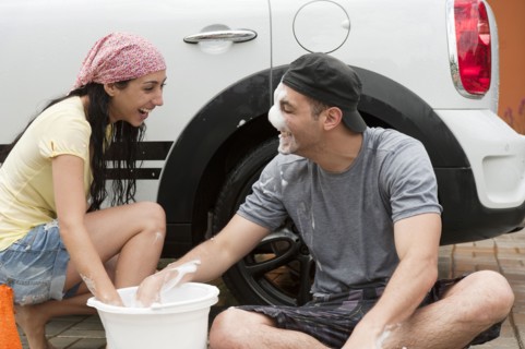 Playful Hispanic couple washing car together