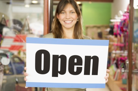 Hispanic woman holding open sign in store