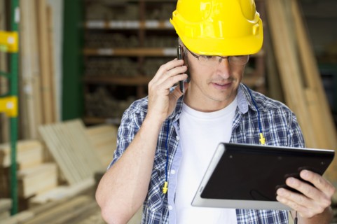 Hispanic carpenter using cell phone and digital tablet