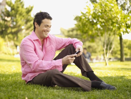 Man sitting in grass text messaging in park
