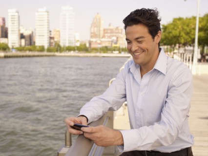 Man at waterfront text messaging on cell phone