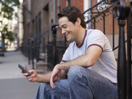 Man on front stoop text messaging on cell phone