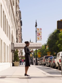 African businesswoman looking at cell phone on sidewalk