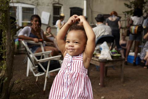 Mixed race baby girl standing on patio with arms raised