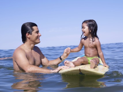 Hispanic father holding hands with daughter on surfboard