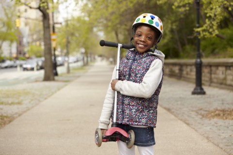 Mixed race girl holding push scooter on sidewalk