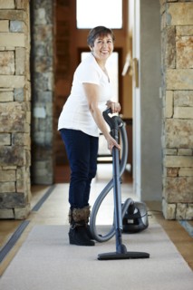 Older Hispanic woman vacuuming carpet