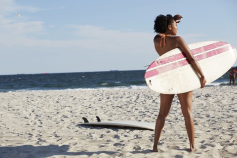Mixed race woman carrying surfboard on beach