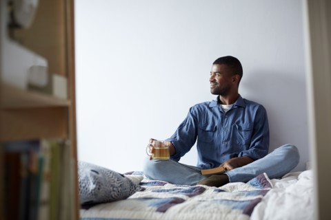 Black man drinking tea and reading on bed