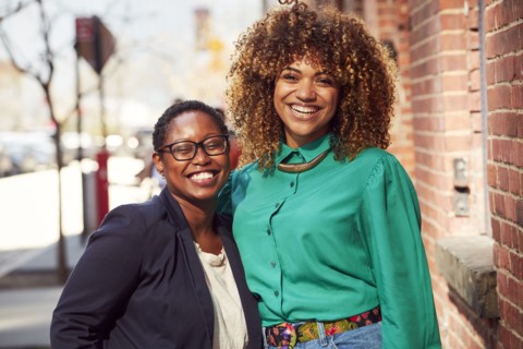 Smiling Black women posing on city sidewalk
