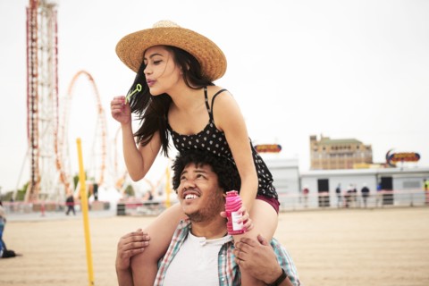 Man carrying woman blowing bubbles on shoulders at beach