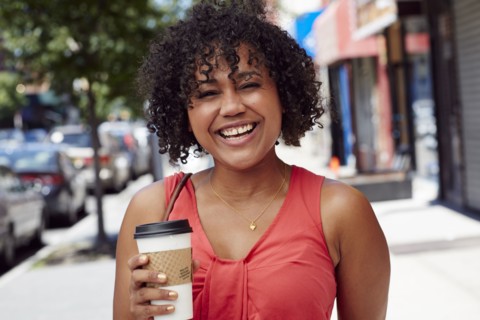 Smiling woman carrying coffee on city sidewalk
