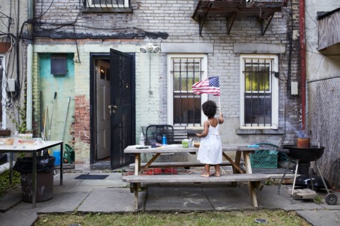 Mixed Race girl standing on backyard bench waving American flag