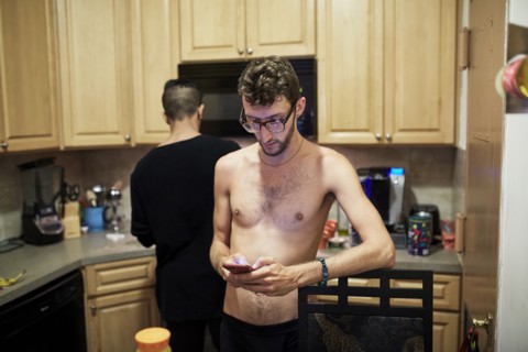 Man with bare chest texting on cell phone in kitchen