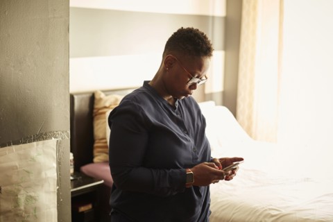 Black woman standing in bedroom texting on cell phone