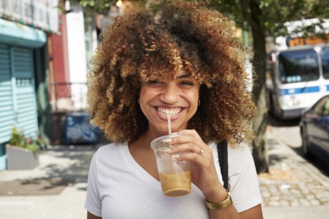 Black woman drinking with straw on city sidewalk