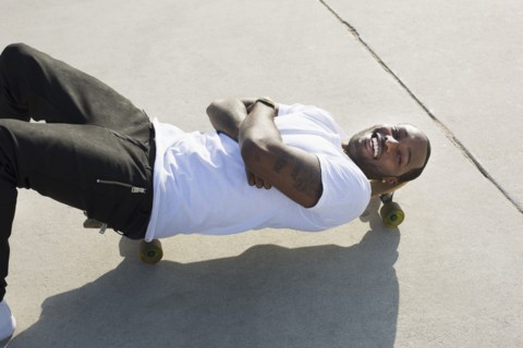African American man laying on skateboard on city street