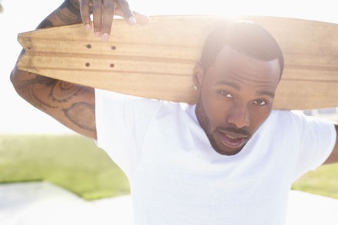 African American man carrying skateboard outdoors