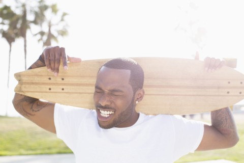 African American man carrying skateboard outdoors