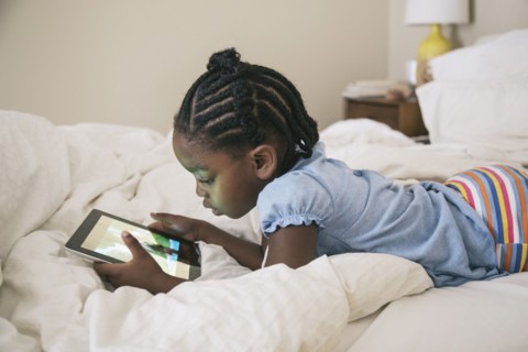 African American girl using digital tablet on bed