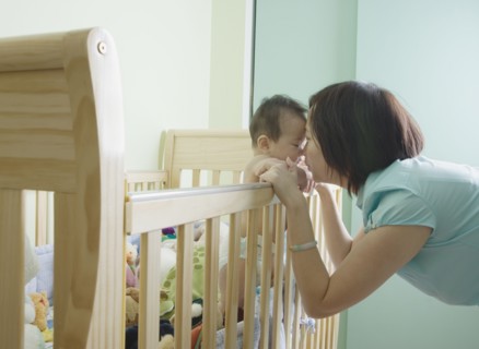 Asian mother and baby touching noses over crib