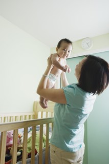 Asian mother lifting baby out of crib