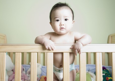 Asian baby standing in crib