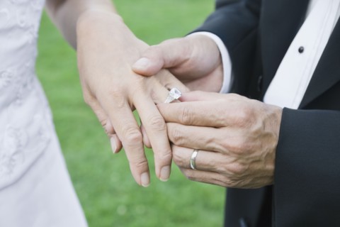 Asian groom putting ring on bride's finger