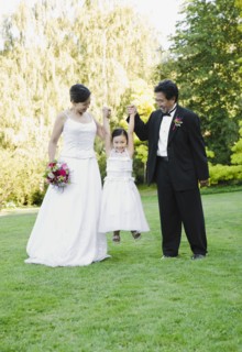 Asian newlyweds holding flower girl's hands