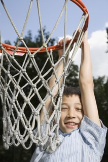 Asian boy hanging from basketball hoop