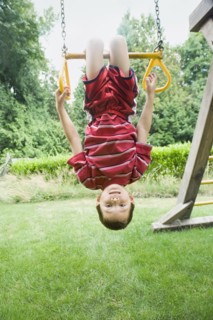 Asian boy hanging upside down on play structure
