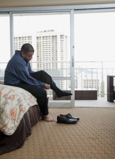 Mixed race man putting socks and shoes on at end of bed