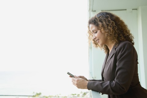 Hispanic woman text messaging on balcony