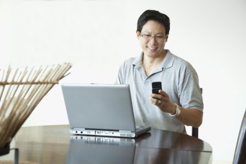 Japanese man using laptop and checking cell phone at table