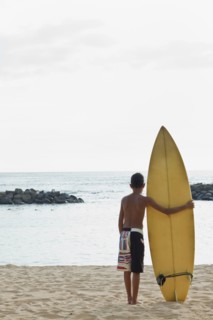 Mixed race boy on beach with surfboard