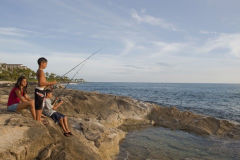 Mixed race children fishing in ocean