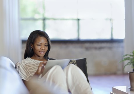 Black woman using digital table on sofa in living room