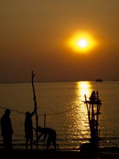 Silhouettes of men standing near river at sunset