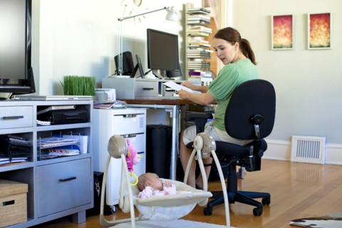 Caucasian mother working in home office with baby next to her